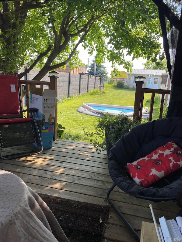 Une terrasse en bois avec un trampoline, une piscine et une chaise dotée d’un coussin à motifs floraux.