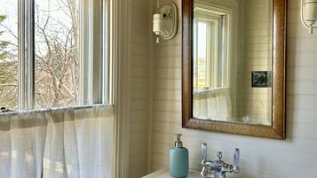 Une salle de bain avec un lavabo blanc, un miroir avec un cadre en bois, un porte-serviettes et une fenêtre avec un rideau.