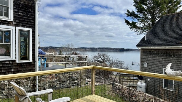 A deck with Adirondack chairs, a view of a lake, and a building with a gray exterior. - Shackford House in Eastport (Eastport)
