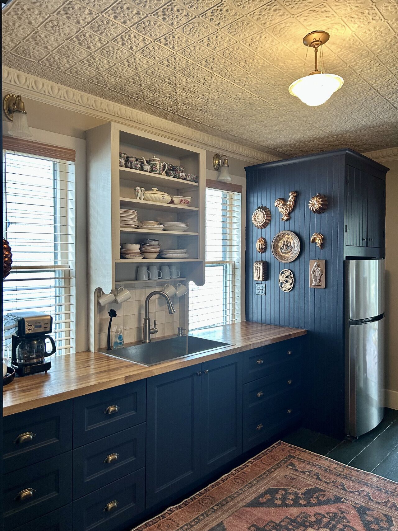 Une cuisine avec des meubles de couleur bleu foncé, un réfrigérateur en acier inoxydable et des plaques murales décoratives.