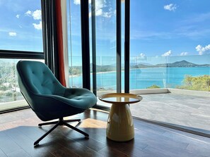 A modern room with a view of a coastal landscape, a teal chair, and a small wooden table. - Luxury 4BR Sea View Villa Chaweng Koh Samui Pool Daily Housekeeping (Koh Samui)