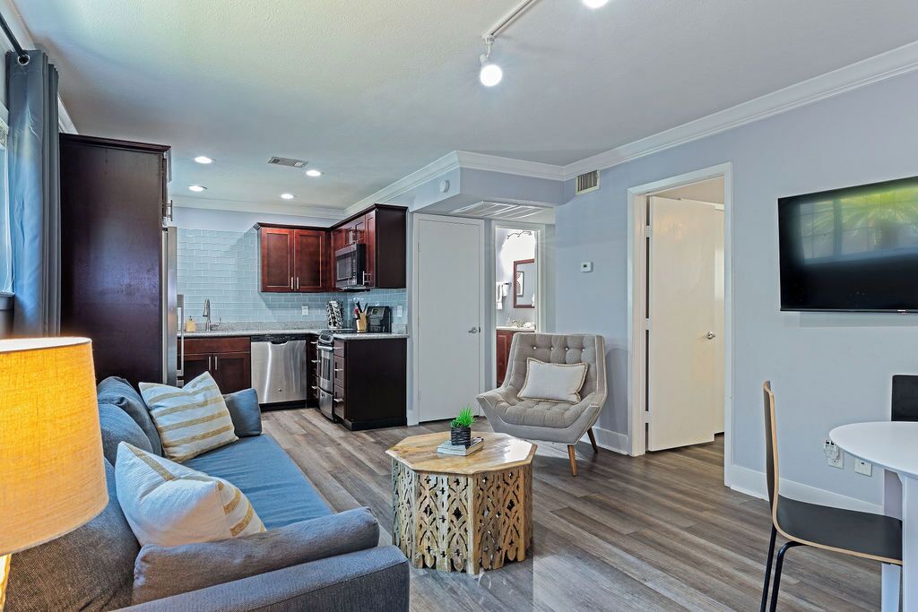 A modern living room with a sofa, coffee table, and TV. It includes a kitchen area with cabinets and appliances.