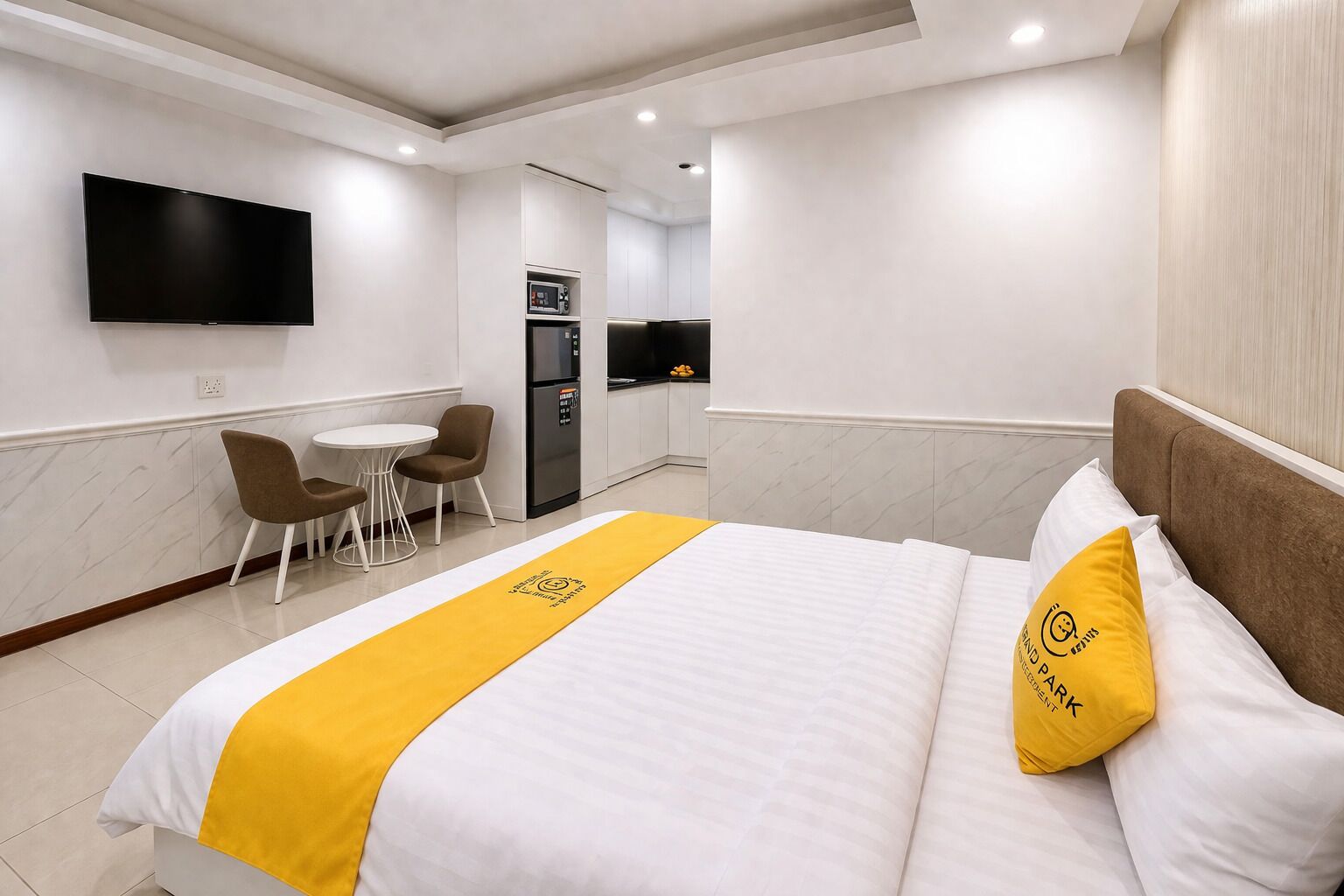 A hotel room with a bed, a TV, a small kitchenette, and a seating area.