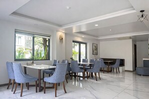 Ein moderner Essbereich mit großem Tisch und Stühlen, großen Fenstern mit Aussicht und einer Decke mit eingelassener Beleuchtung.