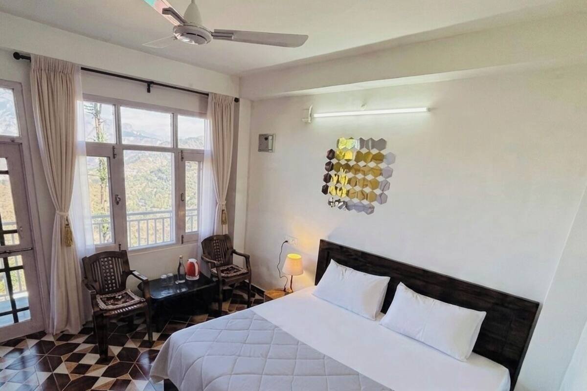 A hotel room with a bed, a desk, a chair, a ceiling fan, and a wall-mounted light fixture.