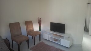 Una sala de estar con dos sillones marrones, un mueble blanco para televisor y una alfombra rosa.