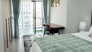 Quarto de hotel com cama, escrivaninha, cadeira, luminária e vista através de uma porta de vidro.