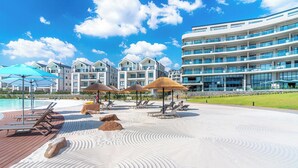 Um resort com piscina, espreguiçadeiras, guarda-sóis e um prédio grande com varandas.