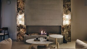Ein stilvoller Lounge-Bereich mit Steinwand, Kamin und zwei runden Tischen mit Weingläsern und einer Weinflasche.