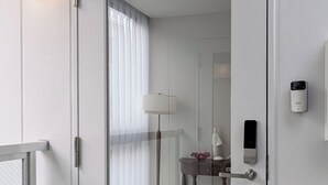 Ein modernes Hotelzimmer mit Glastür, Nachttisch mit Lampe, kleiner Statue und einem an der Wand befestigten Sicherheitssystem.