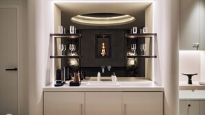 Ein modernes Badezimmer mit einem zentralen Waschbecken, zwei Ablagen mit Gläsern, einem Spiegel und einer dekorativen Leuchte.