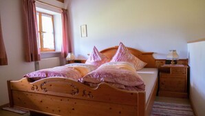 Una cama de madera con cabecera, una mesita de noche con lámpara, una ventana con cortinas y un radiador.