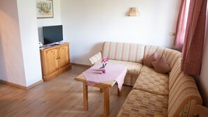 Una sala de estar con un sofá, un mueble de madera, un televisor y una pequeña mesa con un mantel rosa.