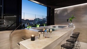 Uma área de bar moderna com vista para a cidade, uma banheira de hidromassagem e uma vela.