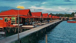 A row of red-roofed overwater bungalows connected by a wooden walkway over water. - SEA WIN HOLIDAY (Mabul Island)