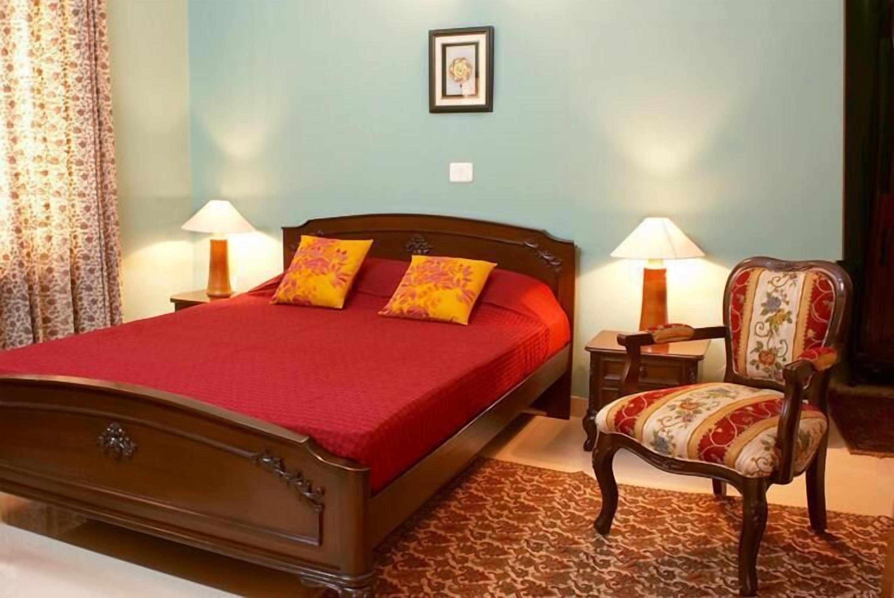Een slaapkamer met een houten bed, twee bedlampjes, een stoel en een ingelijst schilderij aan de muur.
