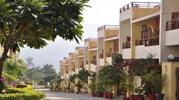 A row of multi-story buildings with balconies, surrounded by potted plants and trees. - Ayurveda Bhavan (Rishikesh)
