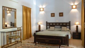 A bedroom with a bed, bedside tables, a mirror, and a bench. - Ayurveda Bhavan (Rishikesh)
