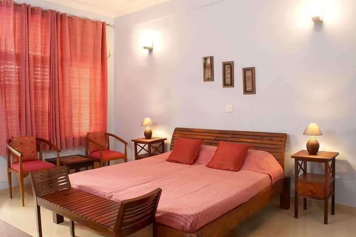 A bedroom with a bed, two chairs, a table, and two bedside tables with lamps.