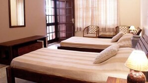 A bedroom with two beds, a chair, a desk, and a window with curtains. - Ayurveda Bhavan (Rishikesh)