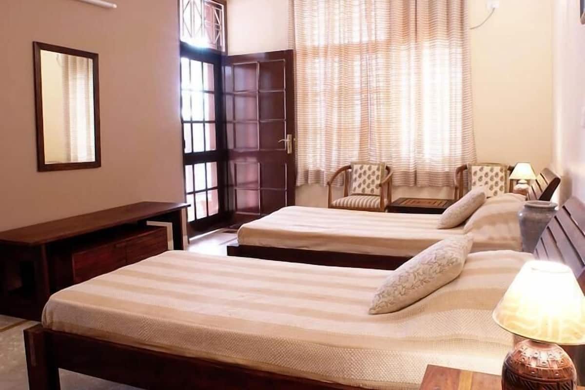 A bedroom with two beds, a chair, a desk, and a window with curtains.