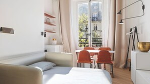 A modern bedroom with a bed, a small table, and a window with a view of buildings. - 345-Tronchet 1G - Stunning Apartment in Paris 8 (Paris)