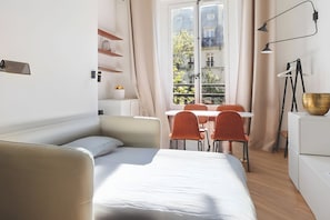 A modern bedroom with a bed, a small table, and a window with a view of buildings. - 345-Tronchet 1G - Stunning Apartment in Paris 8 (Paris)