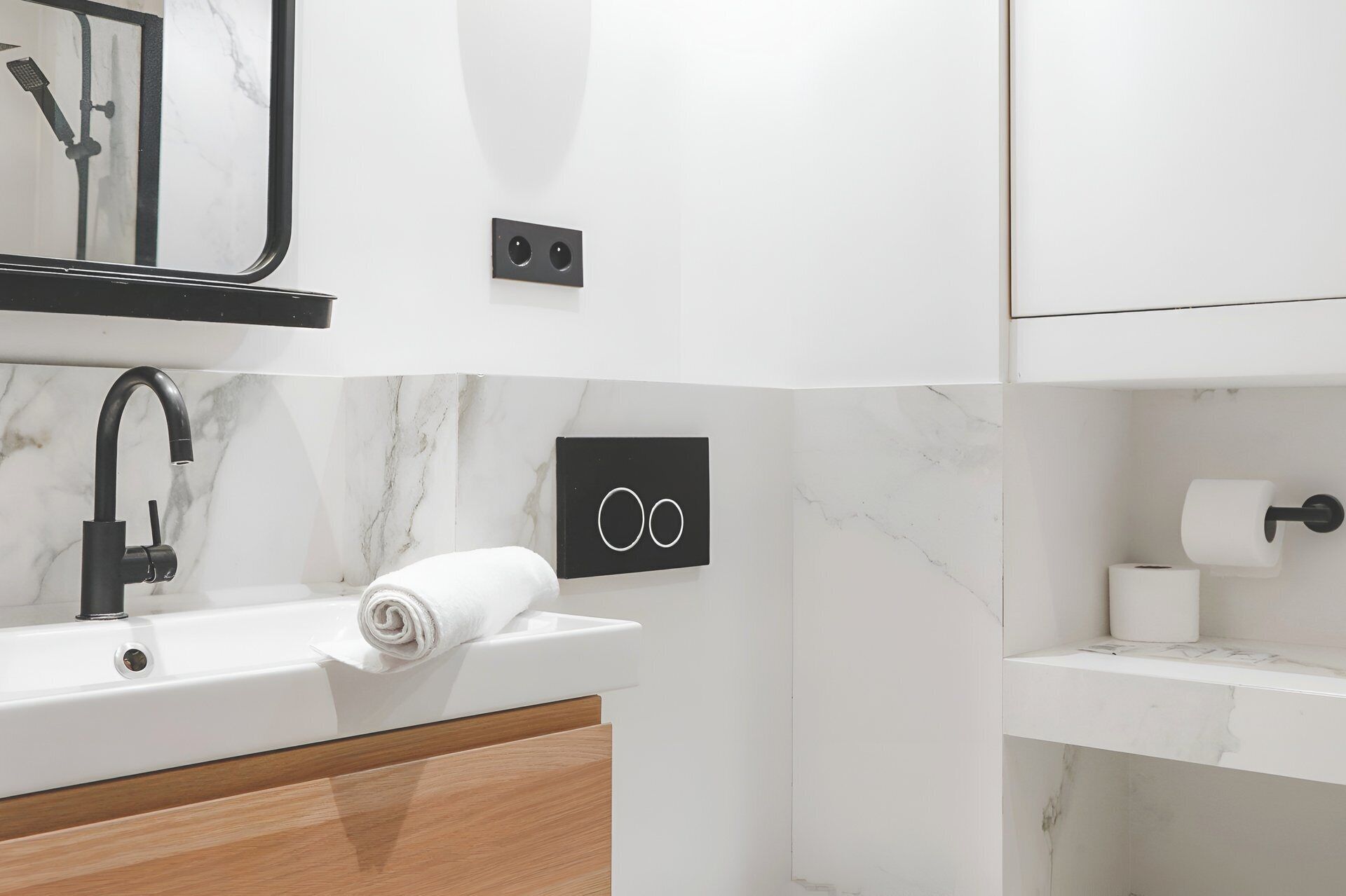 A modern bathroom with a marble sink, a black faucet, a towel, and a toilet paper holder.