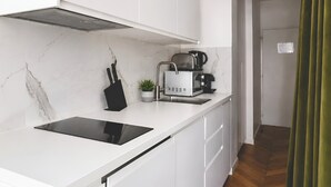 A modern kitchen with white cabinetry, a black induction cooktop, a coffee machine, and a potted plant. - 345-Tronchet 1G - Stunning Apartment in Paris 8 (Paris)