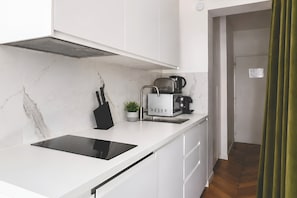 A modern kitchen with white cabinetry, a black induction cooktop, a coffee machine, and a potted plant. - 345-Tronchet 1G - Stunning Apartment in Paris 8 (Paris)