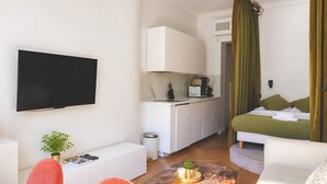 A modern hotel room with a flat-screen TV, a dining area with a coffee machine, a bed with green bedding, and a marble-tiled floor. - 345-Tronchet 1G - Stunning Apartment in Paris 8 (Paris)