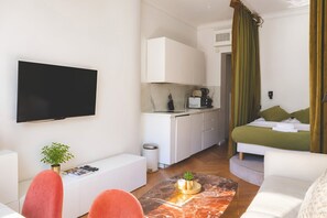 A modern hotel room with a flat-screen TV, a dining area with a coffee machine, a bed with green bedding, and a marble-tiled floor. - 345-Tronchet 1G - Stunning Apartment in Paris 8 (Paris)