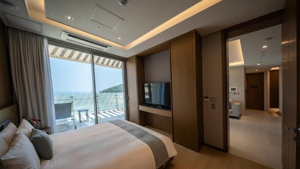 A hotel room with a large bed, a TV, a balcony with a view, and a separate bathroom. - Haeundae Beach Restmons (Busan)
