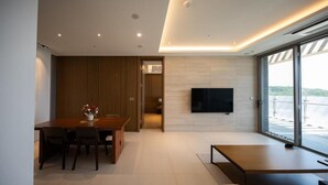 A modern living room with a flat-screen TV, a dining area with a wooden table and chairs, and a large window offering a view. - Haeundae Beach Restmons (Busan)