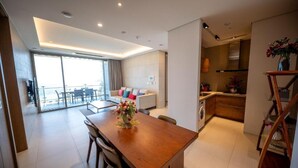 A modern living room with a sofa, a dining table with chairs, a kitchen area, and a balcony with a view. - Haeundae Beach Restmons (Busan)
