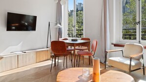 Ett modernt vardagsrum med en platt-TV, ett matbord med stolar, en soffa och stora fönster med gardiner.
