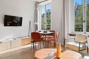 A modern living room with a flat-screen TV, a dining table with chairs, a sofa, and large windows with curtains. - TheBlueStay 346 - Stunning Apartment in Paris 8 (Paris)