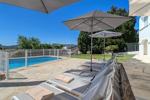 Ein Poolbereich mit Liegestühlen und Sonnenschirmen, einem Schwimmbecken und einer Steinterrasse.