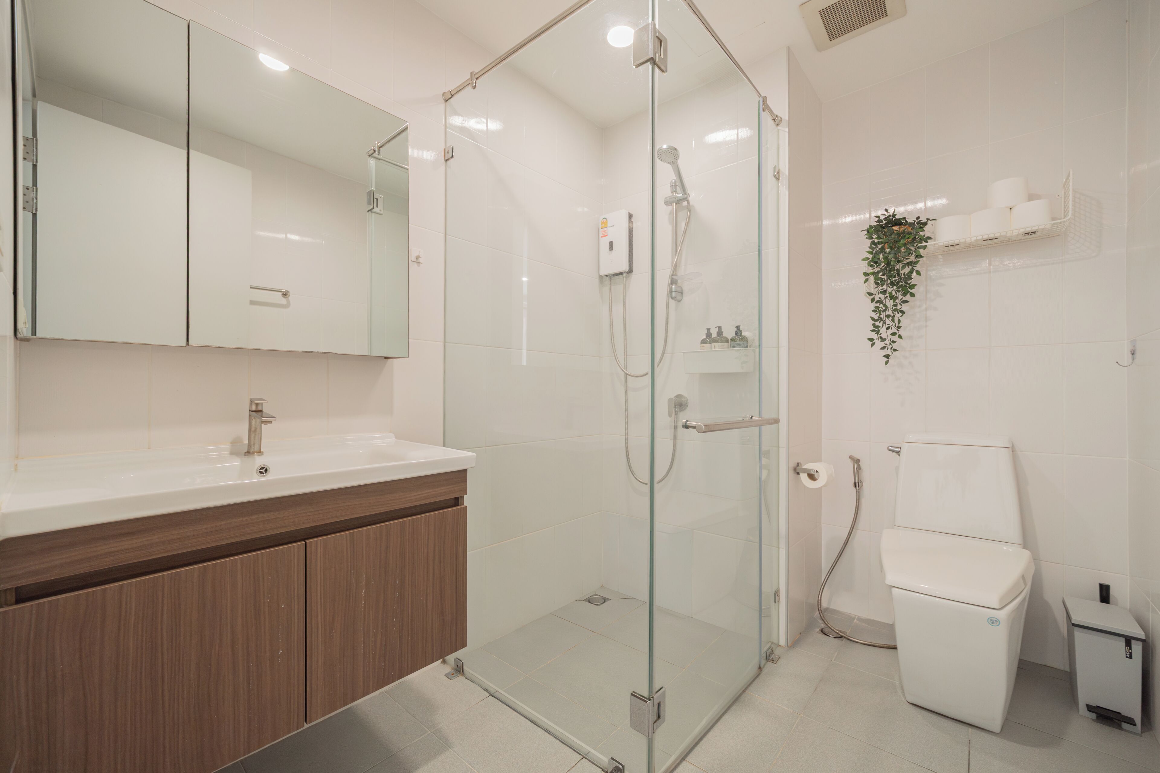 Et moderne badeværelse med en brusekabine med glasdøre, en hvid vask med et træskab og et toilet.