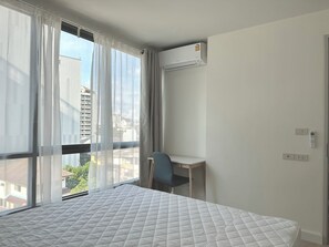 Une chambre d’hôtel avec un lit, un bureau, un climatiseur et une vue sur les immeubles.