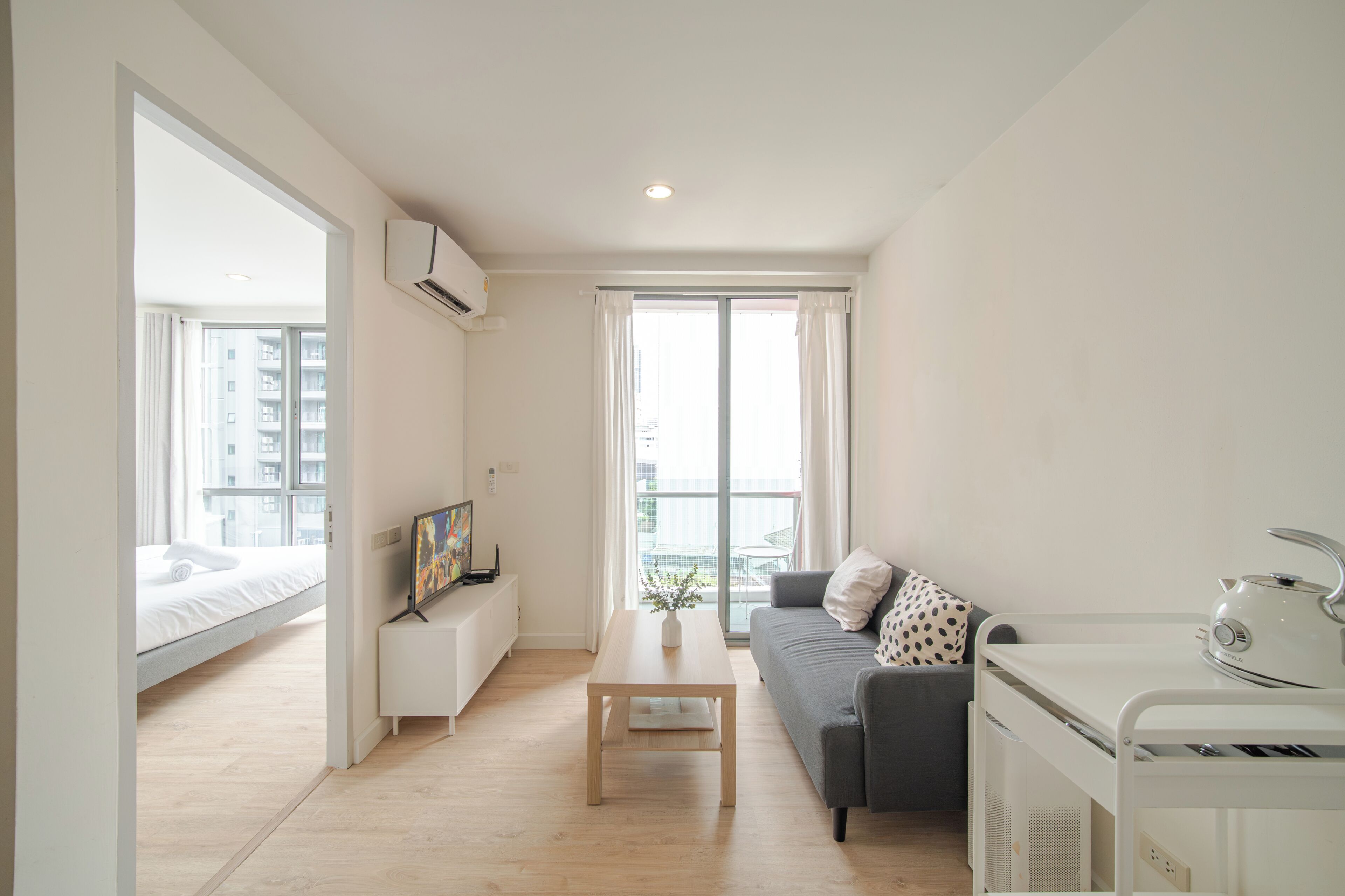 Eine moderne, gut beleuchtete Wohnung mit Bett, Sofa, Couchtisch und Küchenzeile.