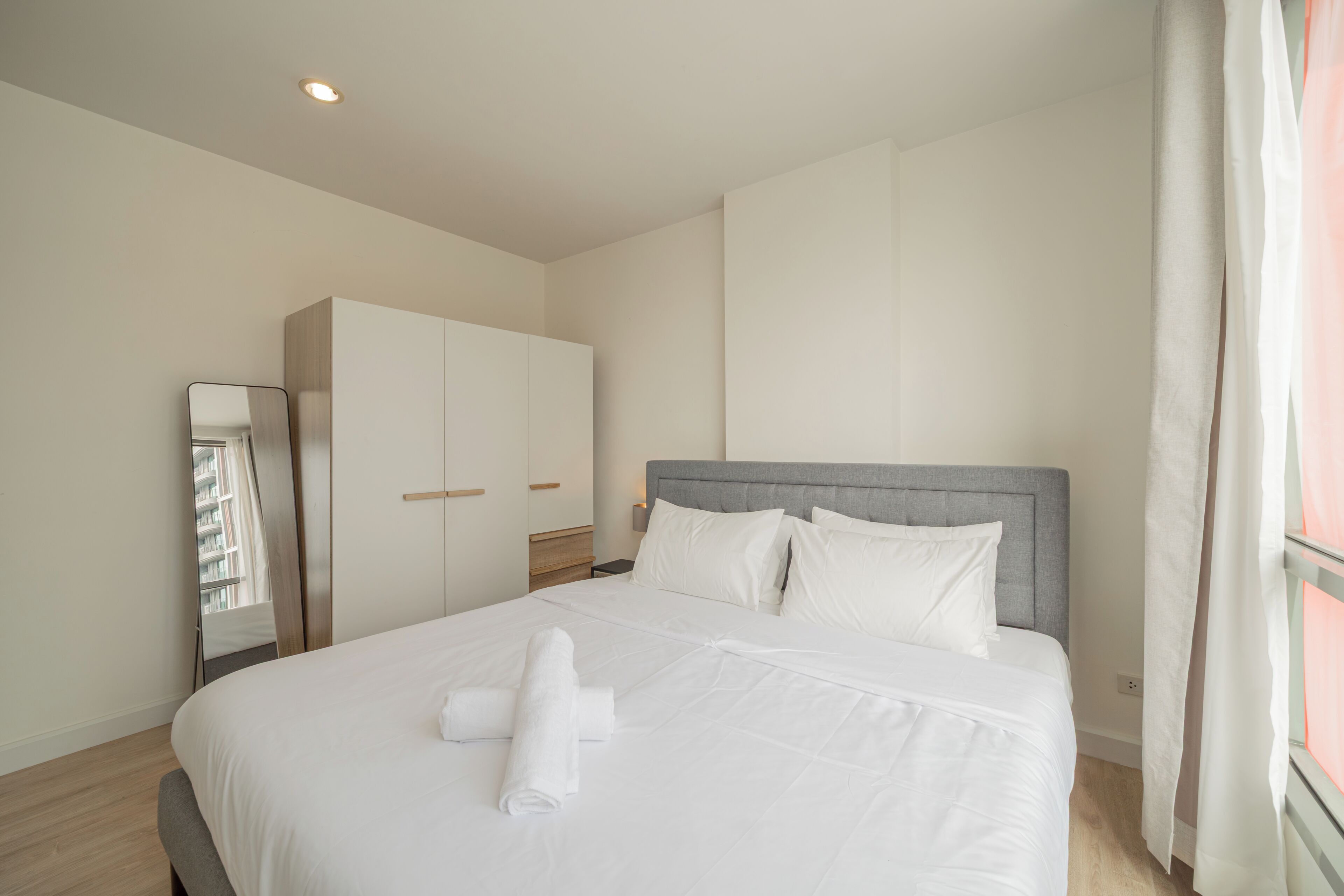 Una habitación de hotel con cama, armario, espejo y ventana con cortinas.