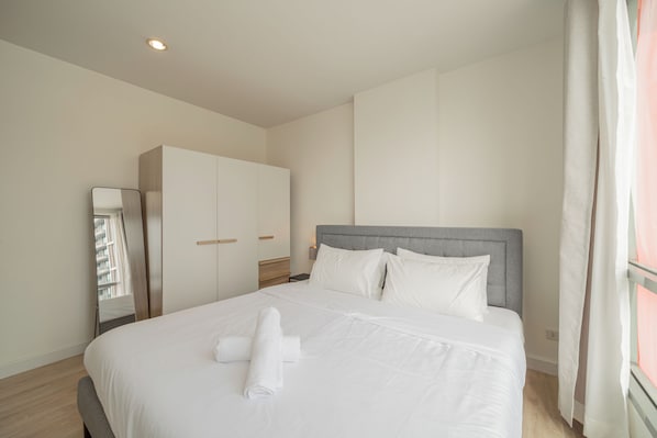 Une chambre d’hôtel avec un lit, une armoire, un miroir et une fenêtre avec des rideaux.