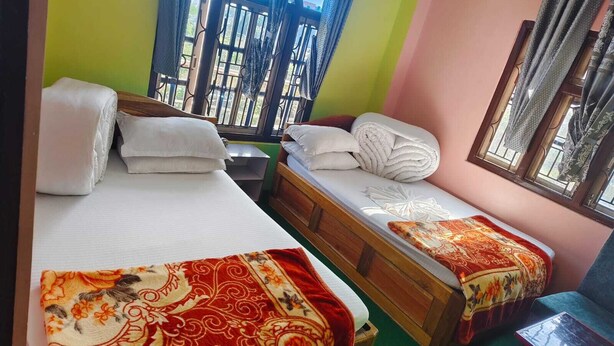 A room with two beds, a small table, and a window with curtains. - Jiyana Hotel and Lodge (Suryodaya)