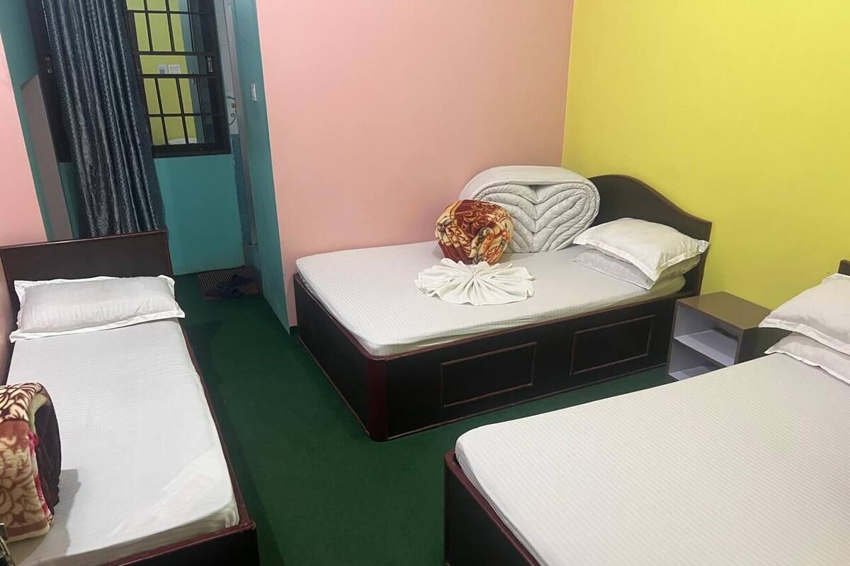 A room with three single beds, a green carpet, and a yellow wall.