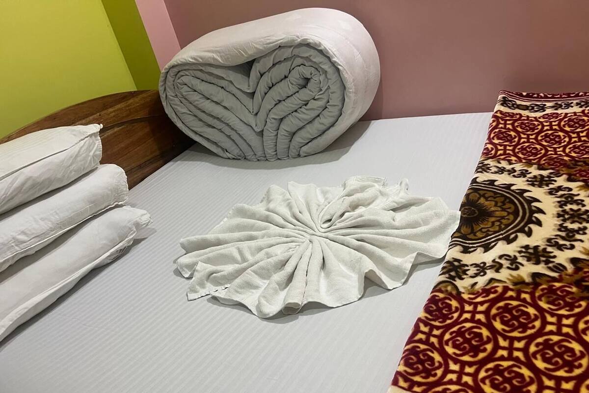 A neatly made bed with a rolled blanket, a decorative towel, and a patterned bedspread.