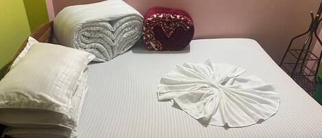 A bed with a striped mattress, a heart-shaped towel, and rolled-up pillows.