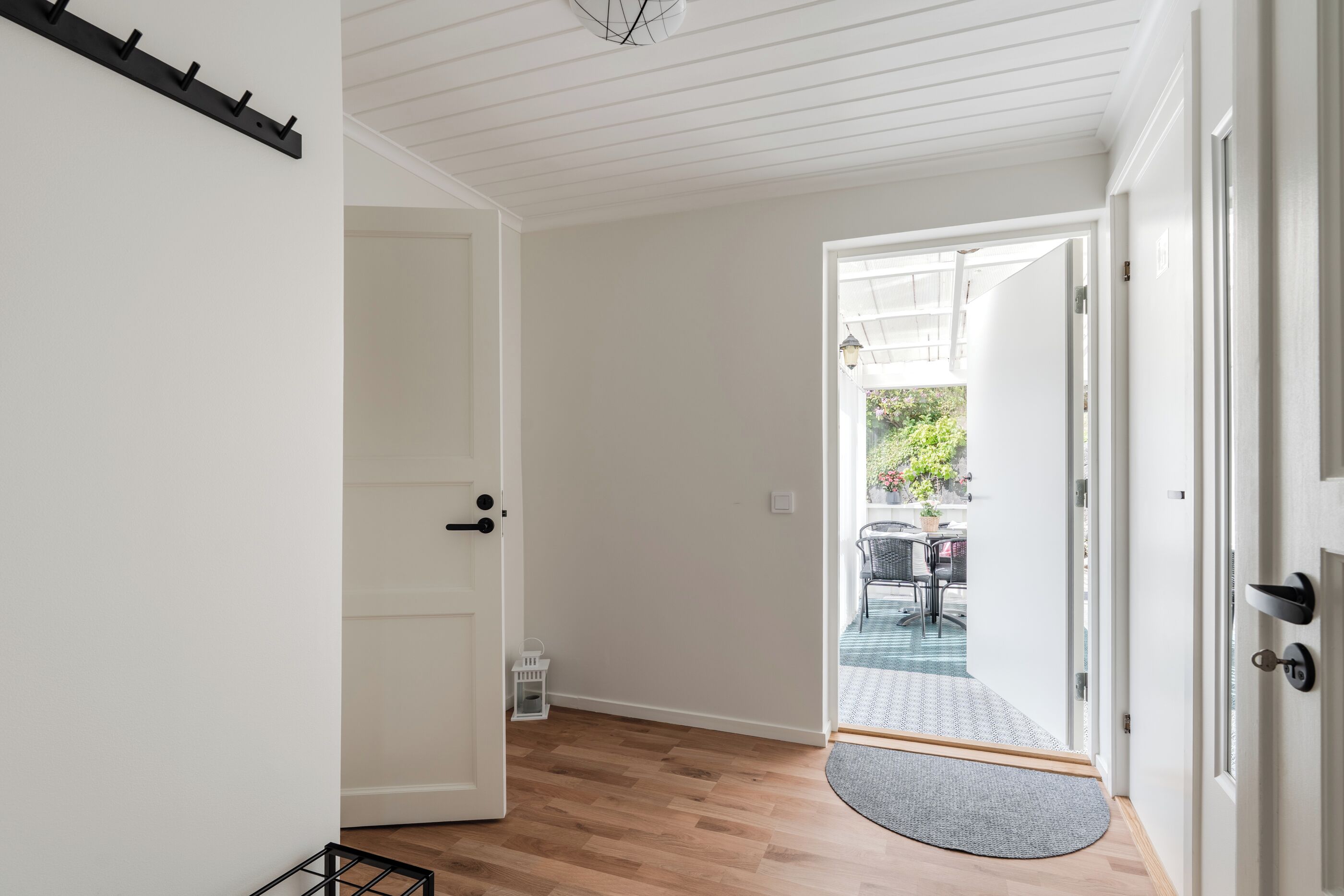 Un couloir doté d’un plancher en bois, de murs blancs et d’une porte donnant sur un espace extérieur aménagé avec une table et des chaises.