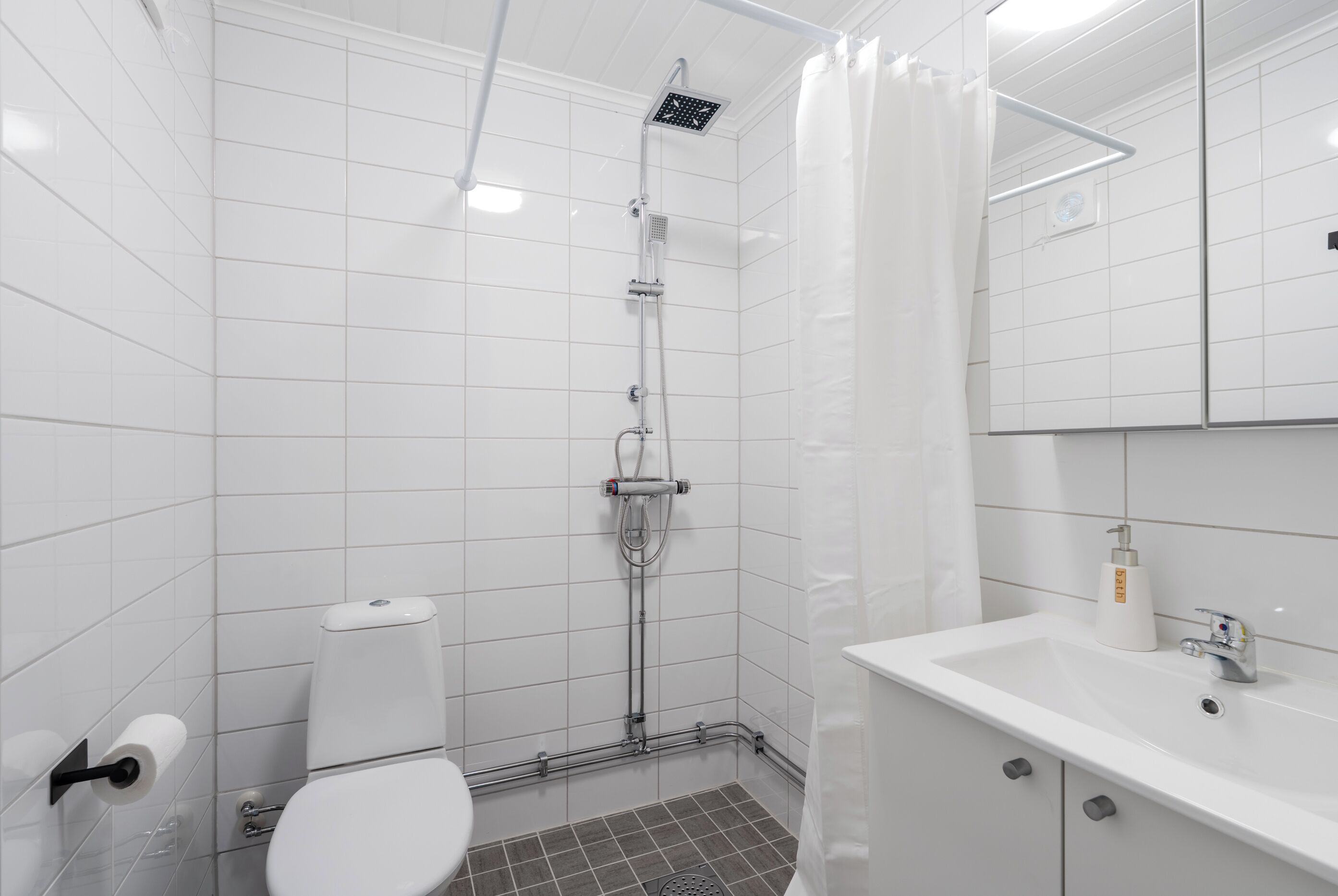 A bathroom with a shower, toilet, sink, and mirror.