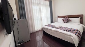 A hotel room with a bed, a television, a refrigerator, and a window with curtains. - HeShan B&B (Hualien City)